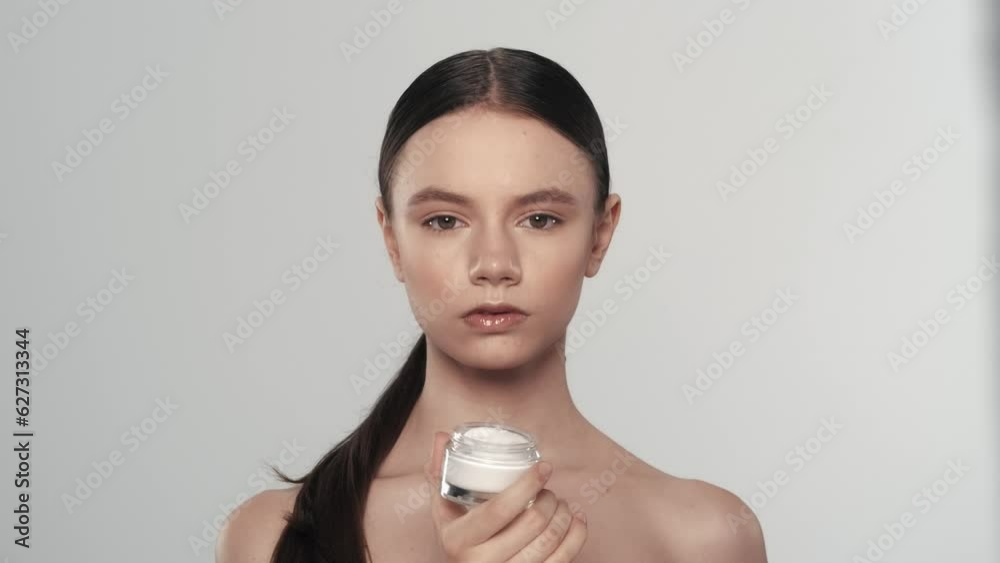 Young woman model with perfect skin holding a small glass jar of cream in hand Young woman model with perfect skin holding a small glass jar of cream in hand