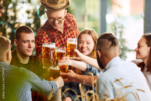 Young smiling people, cheerful friends meeting together in pub, drinking beer, having fun. Celebration, communication. Concept of oktoberfest, traditional taste, friendship, leisure time, enjoyment