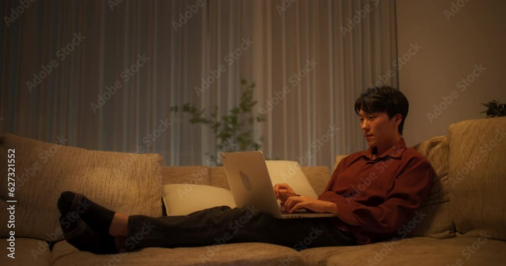 집의 소파에서 노트북으로 블로그 게시물을 작성하는 남성 집의 소파에서 노트북으로 블로그 게시물을 작성하는 남성