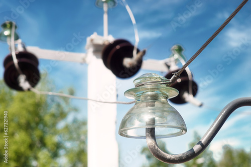 Glass insulator on high voltage pole. Close-up view against sky. High voltage wires. Background.
