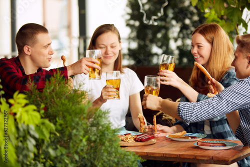 Young people  friends  colleagues meeting at pub in sunny day  drinking lager beer  celebrating  having fun  clinking glasses. Concept of oktoberfest  traditional taste  leisure time  enjoyment