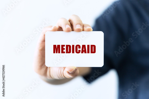 Medicaid text on blank business card being held by a woman's hand with blurred background. Business concept about medicaid.