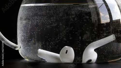 White wireless tws earbud underwater in a glass bowl. The concept of testing the waterproofness and water resistance of wireless headphones. Black background. Photo. Selective focus. photo