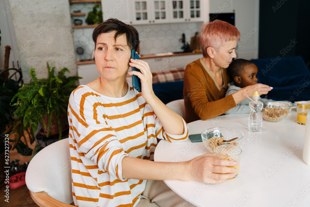 Mature lesbian couple spending with their adopted son in kitchen Mature lesbian couple spending with their adopted son in kitchen