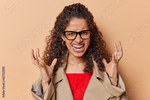Tableau sur toile Irritated curly haired Brazilian woman angrily gestures venting annoyance towards someone her negative emotions are palpable as she stands isolated against brown wall