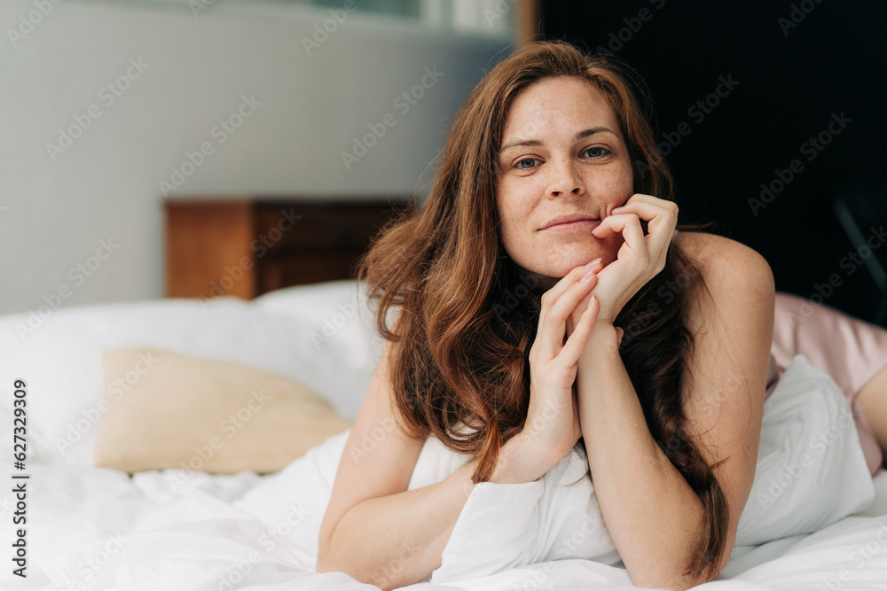 A young beautiful long-haired woman, lying in bed, boredly leaned her head on her hands. A young beautiful long-haired woman, lying in bed, boredly leaned her head on her hands.