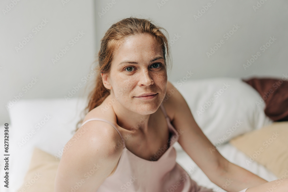 Sunny morning, a young woman with natural authentic beauty sitting on the bed looks at the camera. Sunny morning, a young woman with natural authentic beauty sitting on the bed looks at the camera.