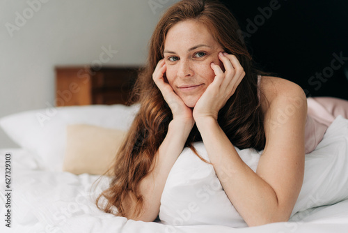 A young beautiful long-haired woman, lying in bed, with head in her hands.