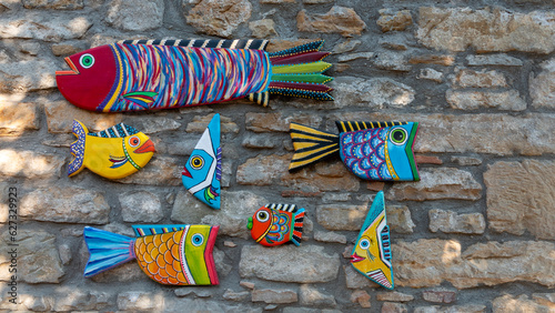 Colorful wooden fish ornaments on the stone wall. Modern Wood Art. Handmade carved from wood
