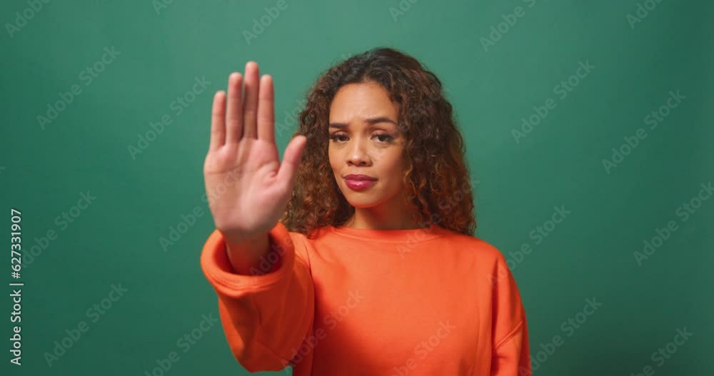 Young multi-ethnic woman holds up hand saying No, Stop, green studio background