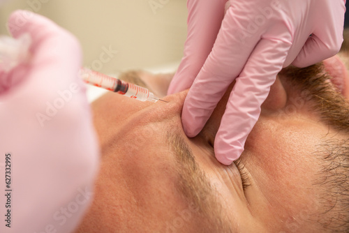 Men's cosmetology. Close up Cosmetologist makes a man the procedure of beauty injection of botulinum toxin in the wrinkles of the forehead and bridge of the nose rejuvenation of a handsome man © Tetiana