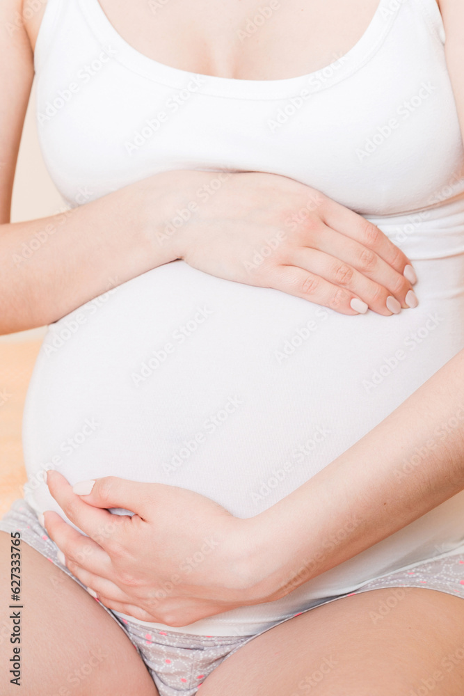 Young pretty pregnant woman, in pain, sitting on bed in bedroom, preparing to give a birth