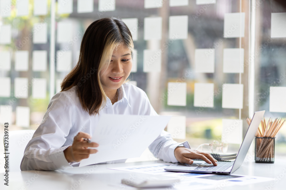 Woman working with laptop and reading business finance report document on office desk. Woman working with laptop and reading business finance report document on office desk.