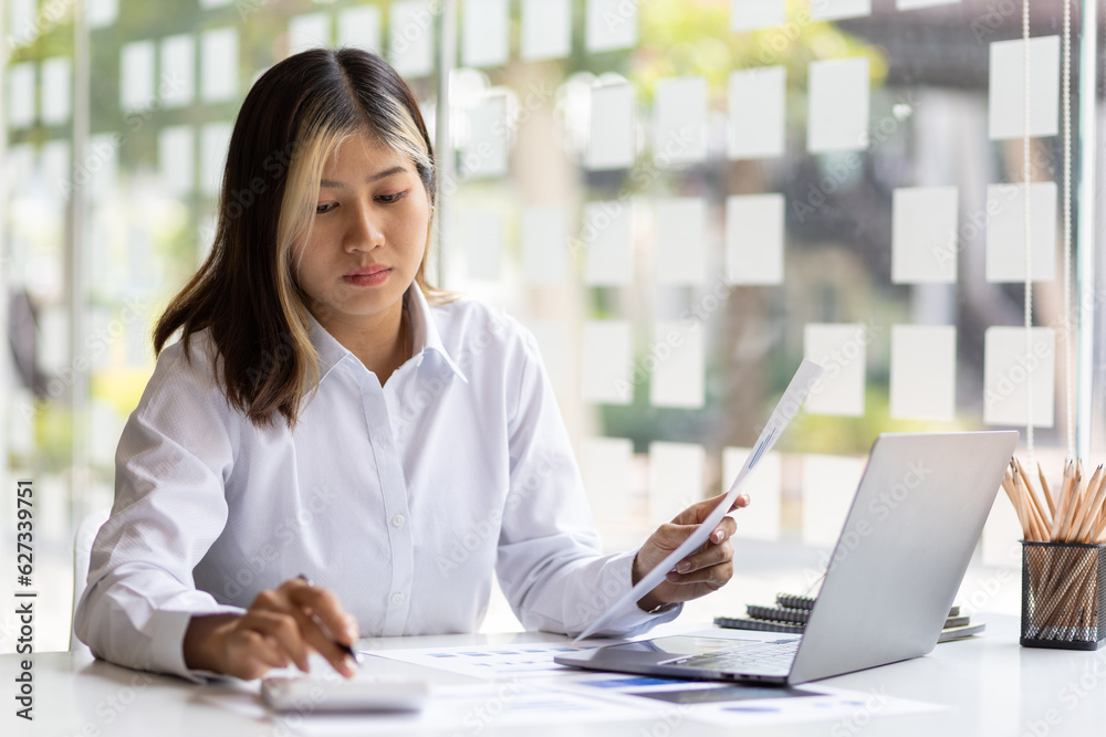 Woman working with laptop and reading business finance report document on office desk. Woman working with laptop and reading business finance report document on office desk.