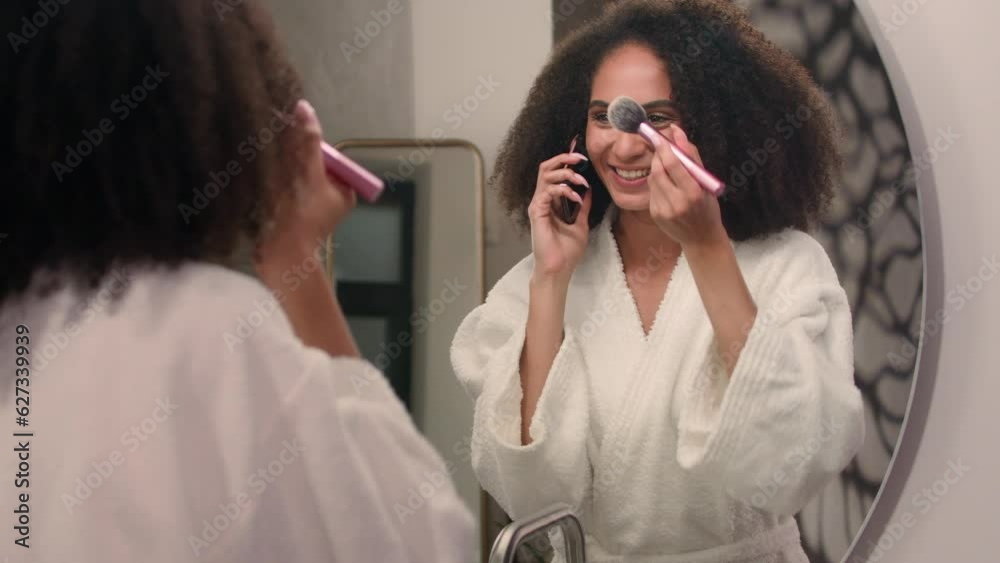 Beautiful African American woman happy smiling girl in bath home looking at mirror reflection apply powder face make up preparing to dating with cosmetics talking phone laughing talk call smartphone Beautiful African American woman happy smiling girl in bath home looking at mirror reflection apply powder face make up preparing to dating with cosmetics talking phone laughing talk call smartphone