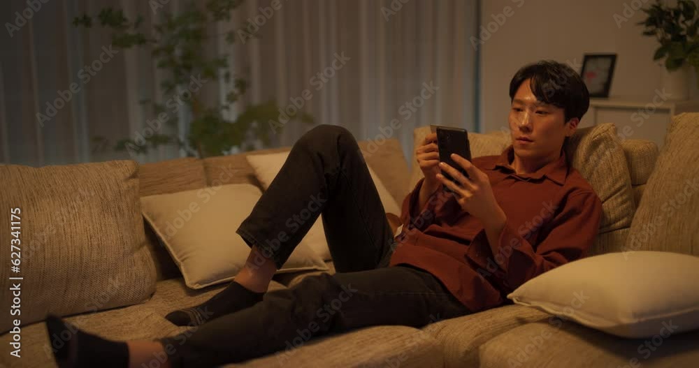 거실에서 스마트폰으로 스트리밍 앱의 구독을 갱신하는 남성 거실에서 스마트폰으로 스트리밍 앱의 구독을 갱신하는 남성