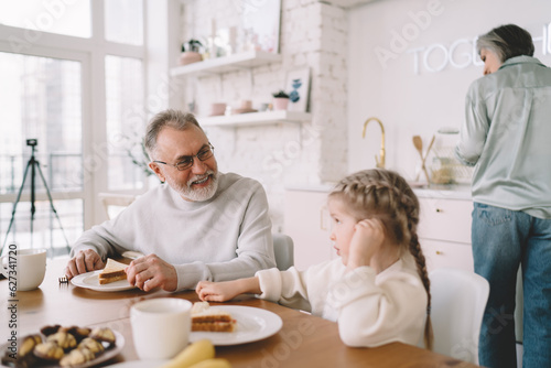 Smiling grandfather and granddaughter eating sandwiches in kitchen