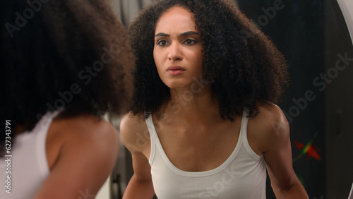 Worried young beautiful African American woman sad ethnic girl looking in mirror stressed about facial wrinkles problem acne frustrated upset touching face dry sensitive skin care facial blackheads
