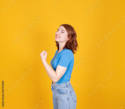 Close up portrait of young red hair nice positive girl showing muscles. Side view attractive charming lovely woman doing girl power gesture. Isolated yellow background, copy space. Lifestyle concept.
