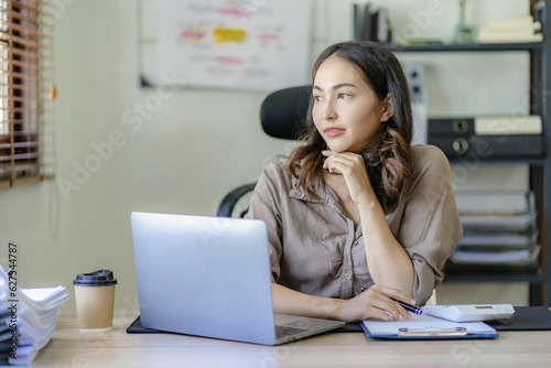 Asian woman working on documents on laptop at work sitting at desk planning financial report business plan investment Financial business analysis and research concepts.