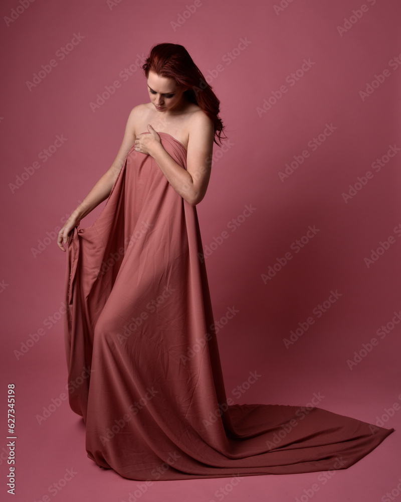 Portait of beautiful woman wearing gown of draped silk fabric, standing pose. Isolated on pink studio background.
