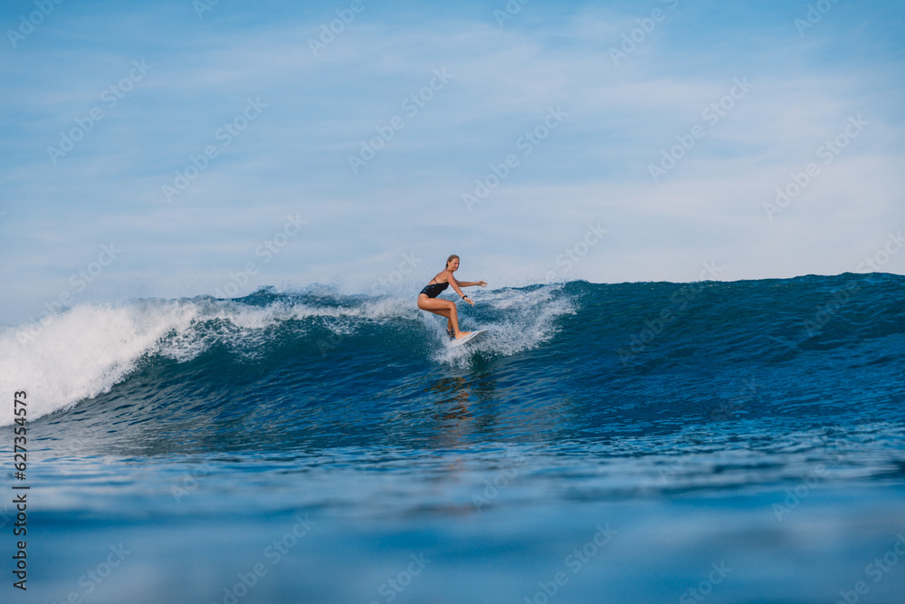 Surfer woman riding on ocean wave on surfboard. Woman during surfing with morning light