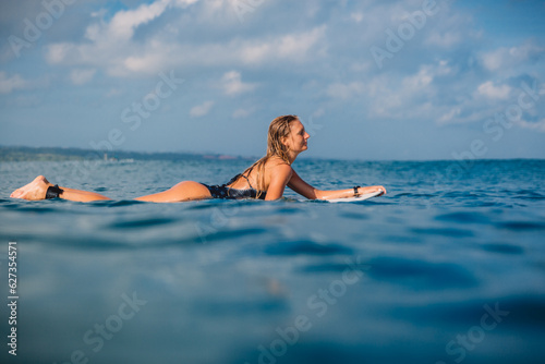 Attractive woman with surfboard. Surfgirl rowing on surfboard in ocean