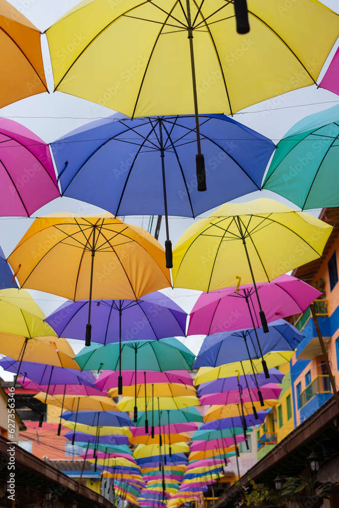 Many bright colorful hanging umbrellas over a small cobblestone pedestrian street in Guatape Colombia - small tourist town near Medellin. Selective focus.