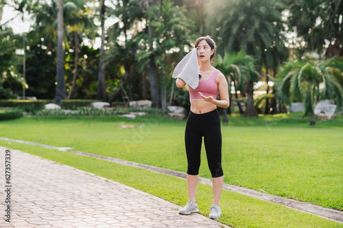 Embrace the beauty of a healthy lifestyle as 30s Asian woman in pink sportswear wipes her cheek after a morning run in the public park. Achieve fitness goals and experience a sense of accomplishment. © Jirawatfoto
