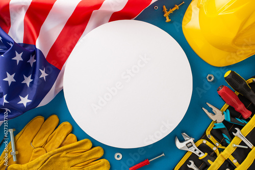 Engage your audience with this construction-themed Labor Day celebration top-down shot, featuring a flag, work helmet, gloves, and toolkit on blue backdrop. Ideal for Labor Day promotions or ads