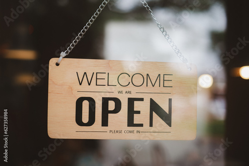 welcome we are open wooden board hanging in front of glass door window of store cafe shop.