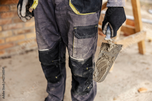 Close up of a housebuilder holding trowel while standing on a building area.