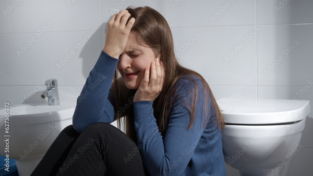 Crying woman suffering from depression sitting on floor in bathroom at home. Concept of depression, suicide, stress, mental illness, loneliness and frustration. Crying woman suffering from depression sitting on floor in bathroom at home. Concept of depression, suicide, stress, mental illness, loneliness and frustration.