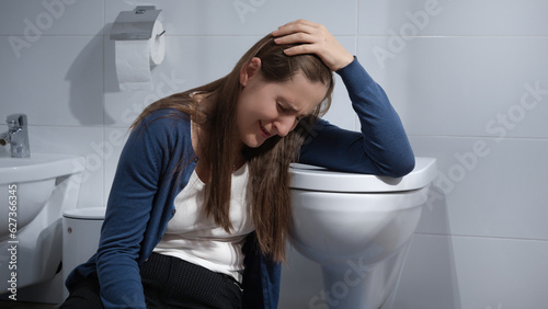 Sad crying woman sitting on floor in bathroom and leaning on toilet