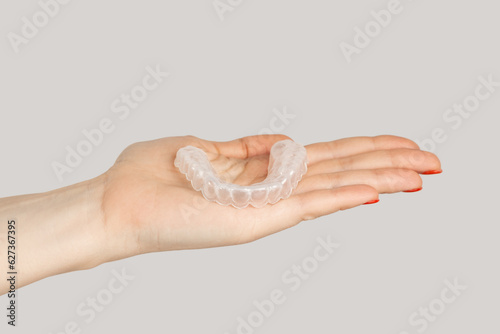 Closeup of woman hand showing invisible orthodontics cosmetic aligners. Indoor studio shot isolated on gray background.