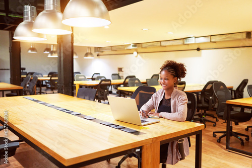 portrait mid adult black woman sitting in office alone working with a laptop smiling