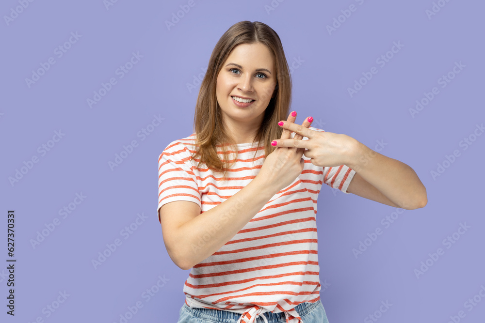 Portrait of blond woman wearing striped T-shirt making hashtag sign with fingers, tagging posts in social networks, recommending tags. Indoor studio shot isolated on purple background. Portrait of blond woman wearing striped T-shirt making hashtag sign with fingers, tagging posts in social networks, recommending tags. Indoor studio shot isolated on purple background.