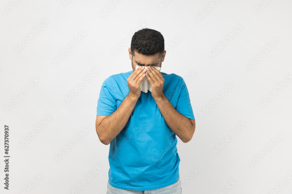 Portrait of stressed offended unshaven man wearing blue T- shirt standing with hand down and crying, expressing sorrow and sadness. Indoor studio shot isolated on gray background. Portrait of stressed offended unshaven man wearing blue T- shirt standing with hand down and crying, expressing sorrow and sadness. Indoor studio shot isolated on gray background.