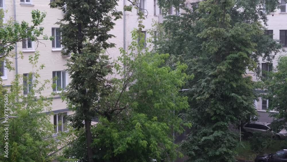 Thunderstorm or heavy rain in the city, raindrops fall on the background of houses and trees Thunderstorm or heavy rain in the city, raindrops fall on the background of houses and trees