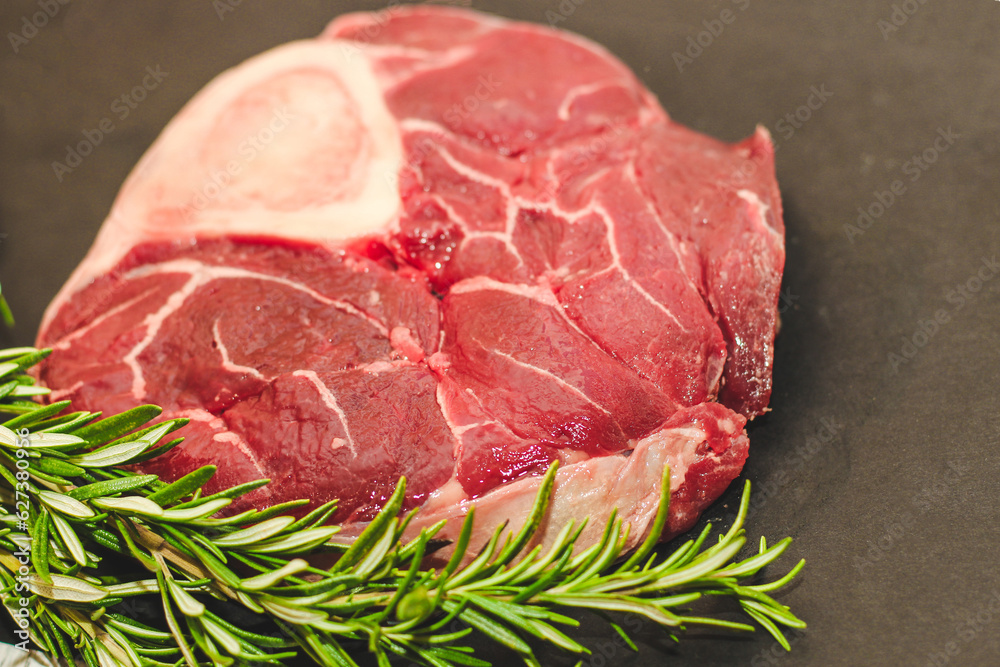 Fresh piece of meat large beef steak on the bone ossobuco with a sprig of rosemary on a black background.