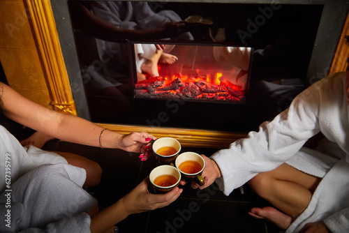 Human hands of men and women with cups of tea by the fireplace. Concept of a friendly indoor gathering