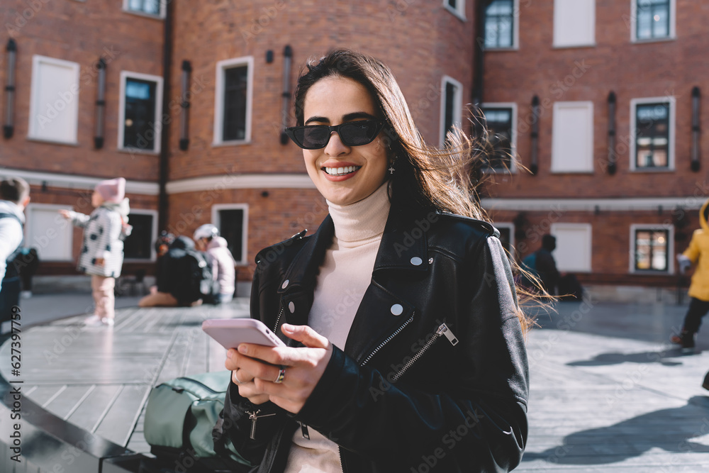 Obraz premium Positive woman smiling and chatting on smartphone on street
