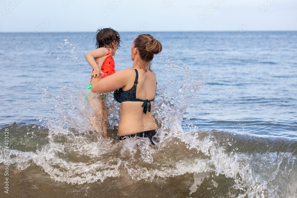 View taken from behind of a mother and daughter playing in the waves of the Pacific Ocean at Kamaole Beach; Maui, Hawaii, United States of America