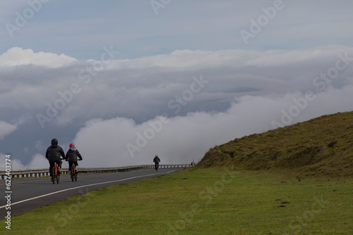 View taken from behind of people bicycling on the paved Road down from Haleakala, enjoying the dramatic views of of the clouds over the Pacific Coast; Maui, Hawaii, United States of America photo