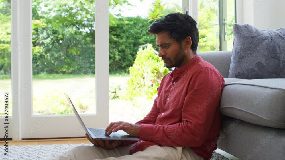 Man working from home sitting on floor leaning against sofa with laptop - shot in slow motion