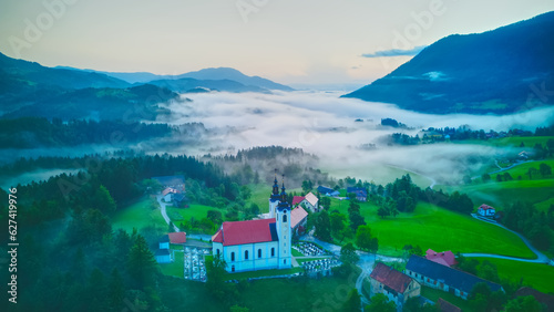 Aerial drone view of small beautiful church on valley in Slovenia at dawn. Beautiful summer morning landscape..