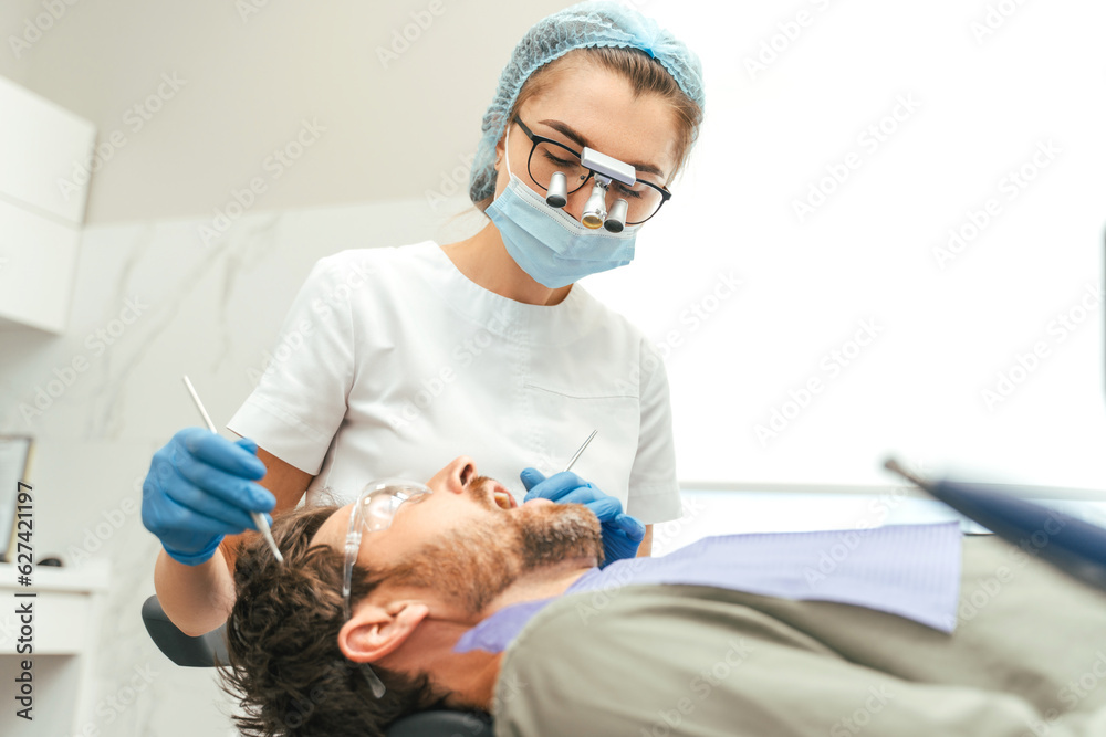 Young bearded man having teeth check up by dentist during appointment Young bearded man having teeth check up by dentist during appointment