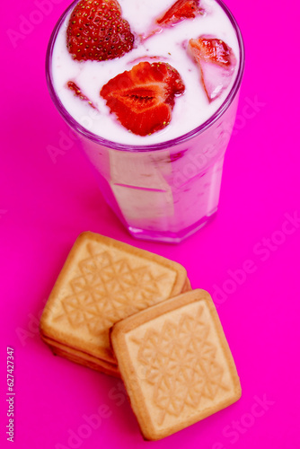 Glass of strawberry yogurt with cookies on pink background. Strawberry yogurt covered by fresh strawberry slices. 