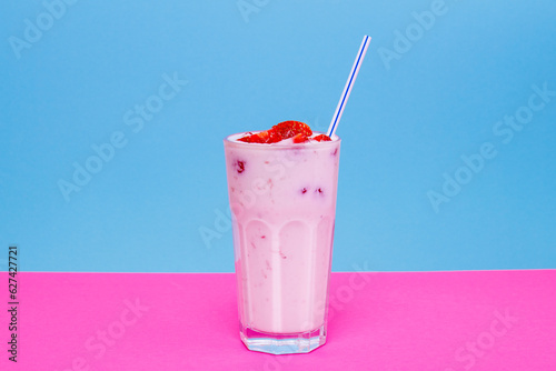 Glass of strawberry yogurt on colorful background. Strawberry yogurt on blue and pink background. Glass of strawberry yogurt covered by fresh strawberry slices. 