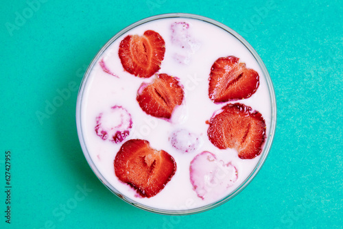 Top view of glass bowl with strawberry yogurt on green background. Strawberry yogurt covered by fresh strawberry slices. 